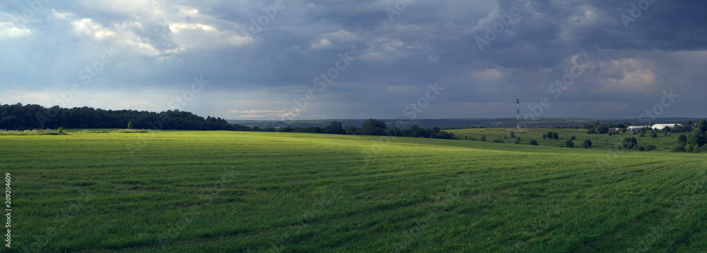 Rural panoramic landscape with sun-lit fielda field, before a thunder-storm.