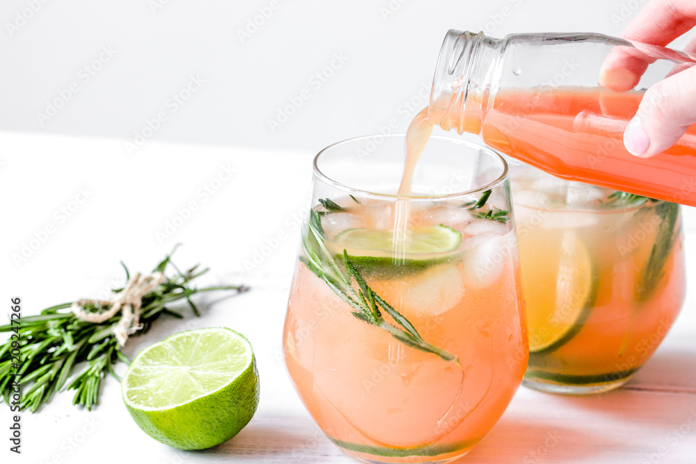 glass of fresh juice with lime and rosemary on white table backg