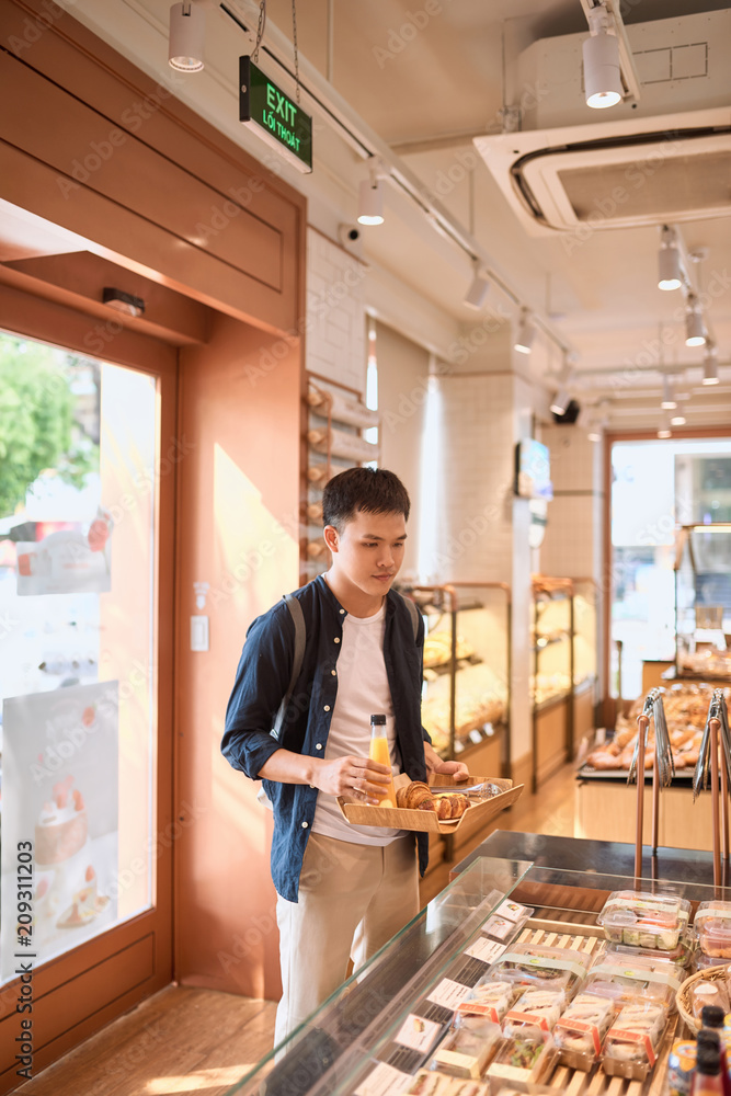 当地面包店的英俊男子拿着装有面包或馅饼的托盘购买甜品