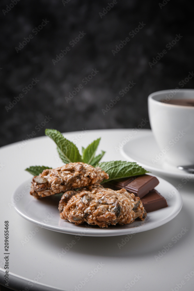 Plate with delicious oatmeal cookies and chocolate on white table against dark background