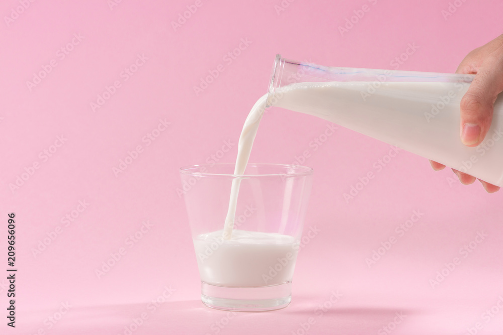 Pouring milk into glass on pink background