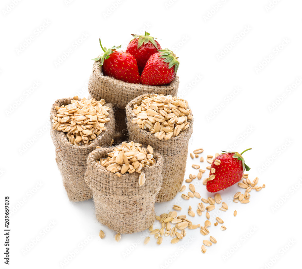 Composition with sacks of raw oatmeal and fresh strawberry on white background