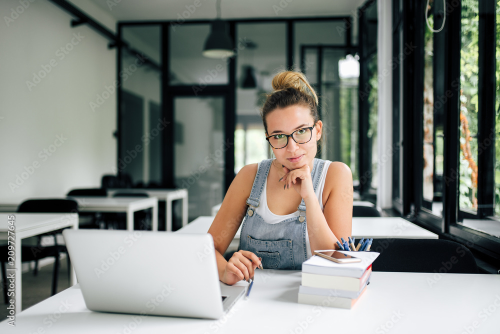 Portrait of charming young female student sitting in modern library.