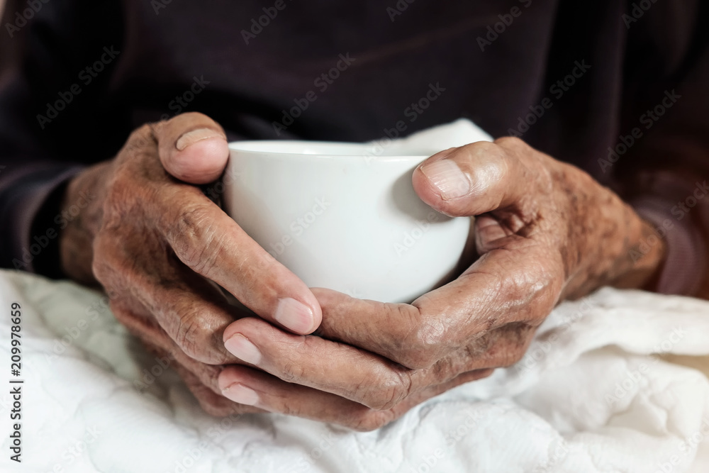 木头桌子上拿着一杯咖啡的老人的手。语调