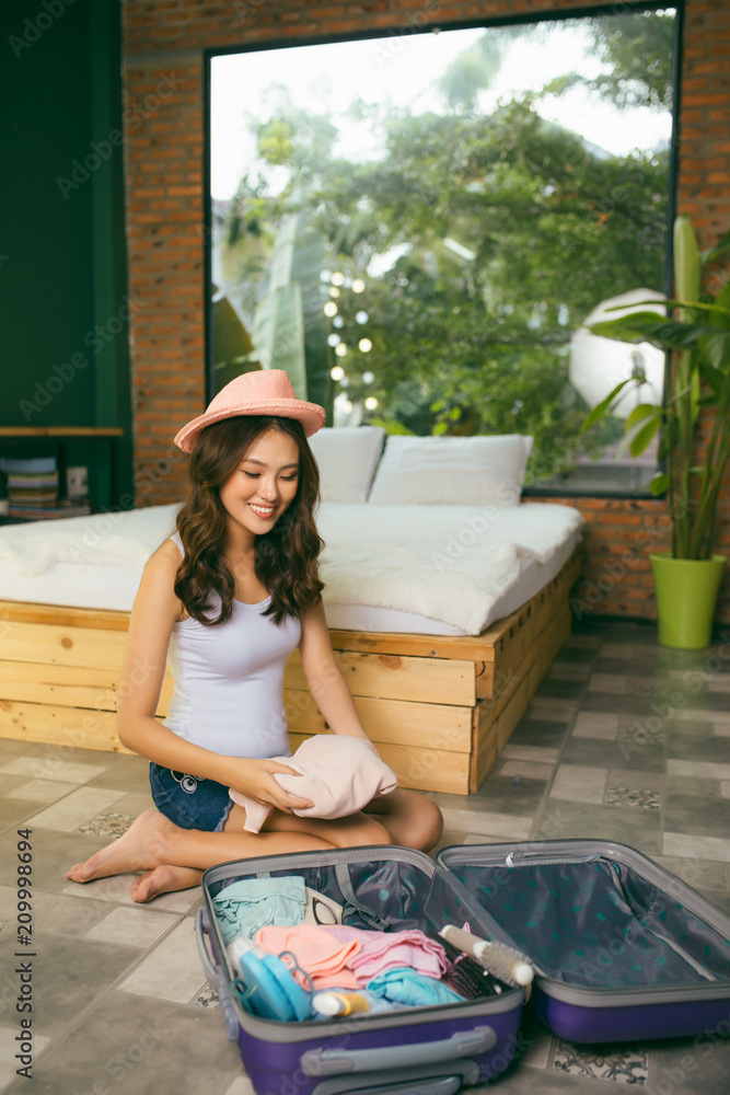 旅行和度假的概念，幸福的女人在床上把东西和很多衣服装进行李箱