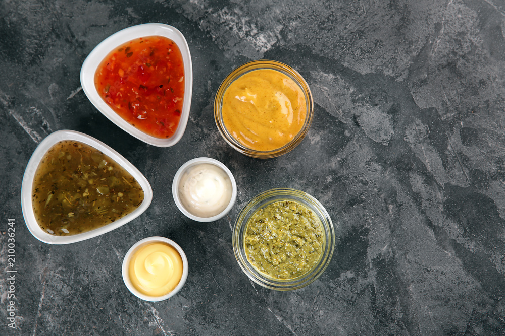 Bowls with different sauces on grey textured background, top view