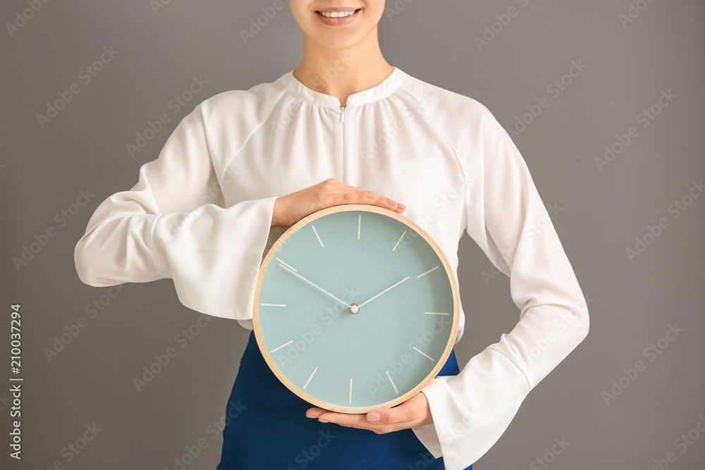 Woman with clock on grey background. Time management concept