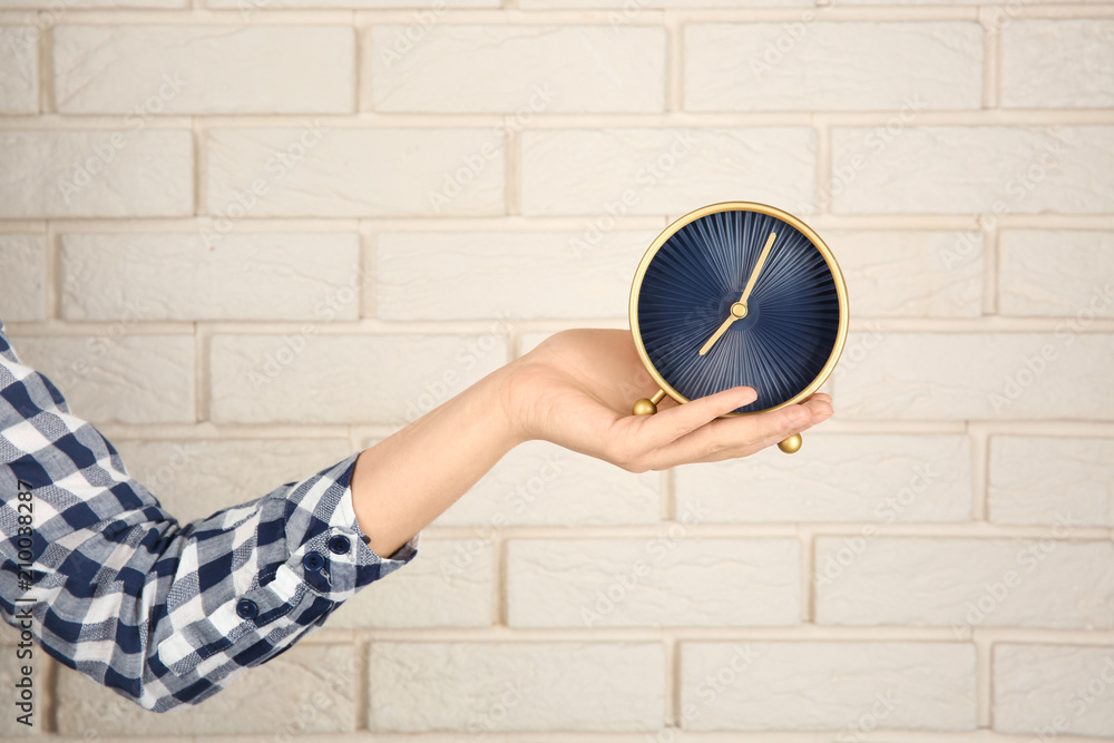 Woman holding clock near brick wall. Time management concept