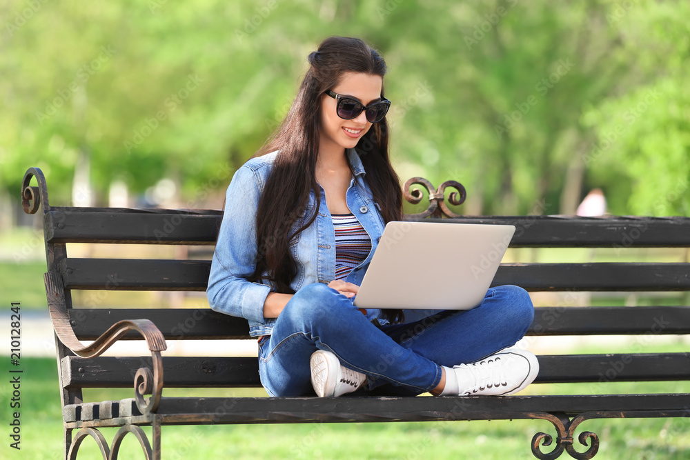 Beautiful young woman resting in park with laptop