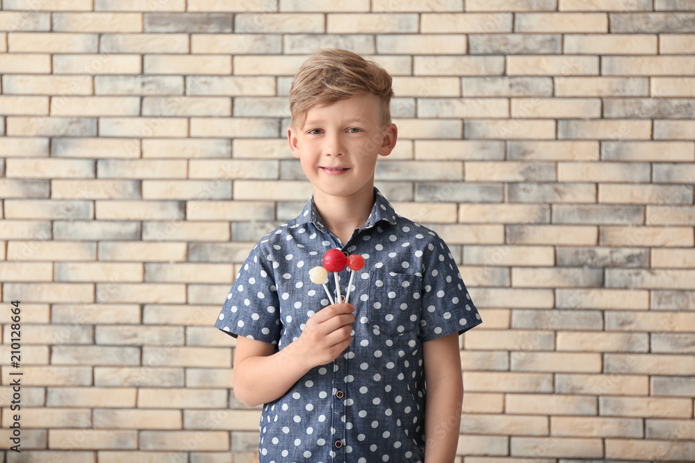 Cute little boy with lollipops near brick wall