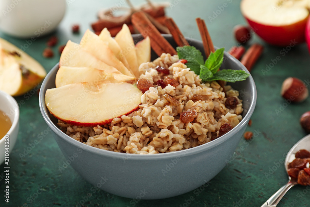 Bowl with tasty oatmeal, fruit and cinnamon sticks on green table, closeup