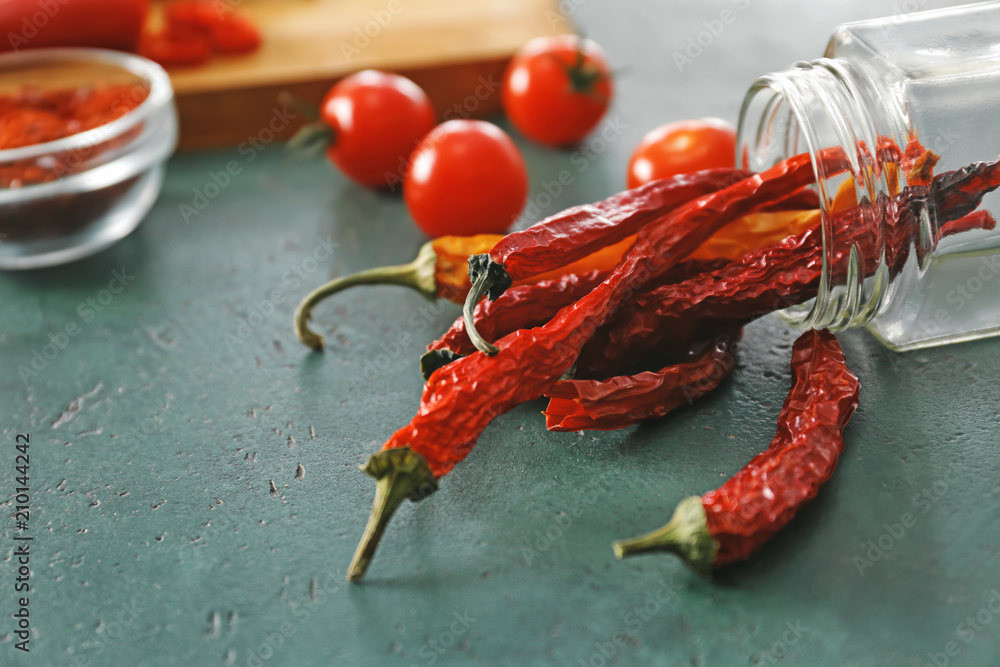 Overturned glass jar with dried chili peppers on green background