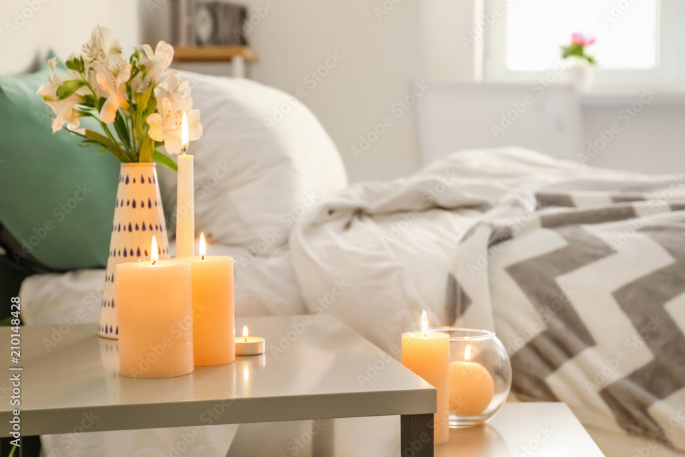 Burning wax candles on table in bedroom