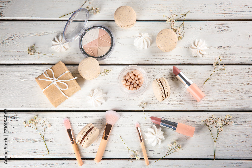 Flat lay composition with tasty macarons and cosmetic products on wooden background