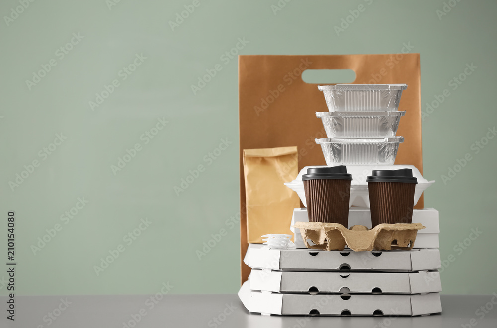 Different packages and carton cups on table against color background. Food delivery service