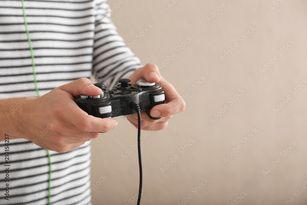 Young man with gamepad on color background