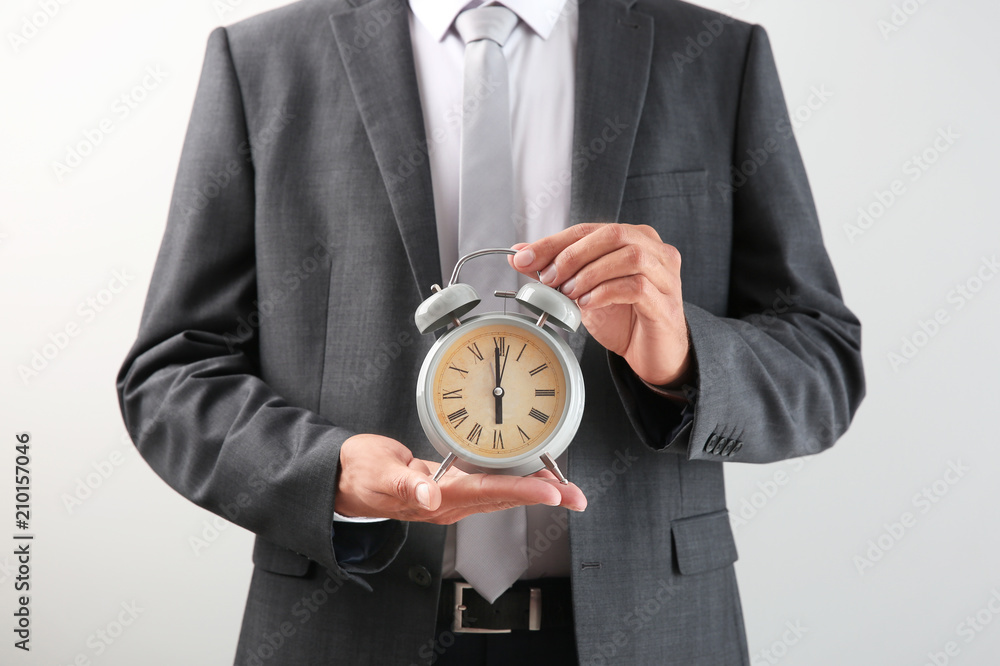 Businessman holding alarm clock on light background. Time management concept