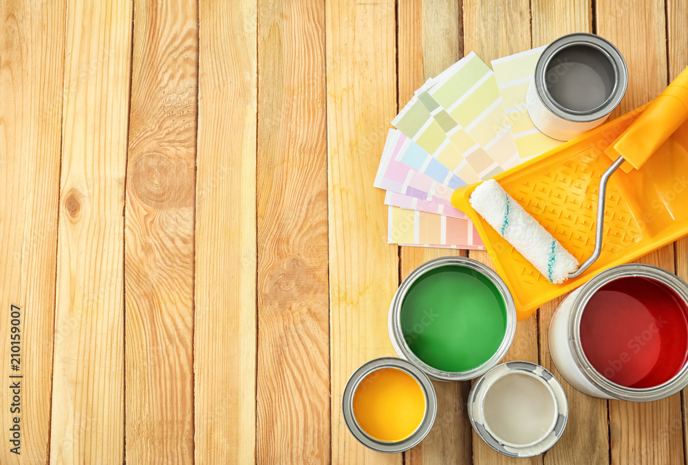 Cans of paint, tray and roller on wooden background