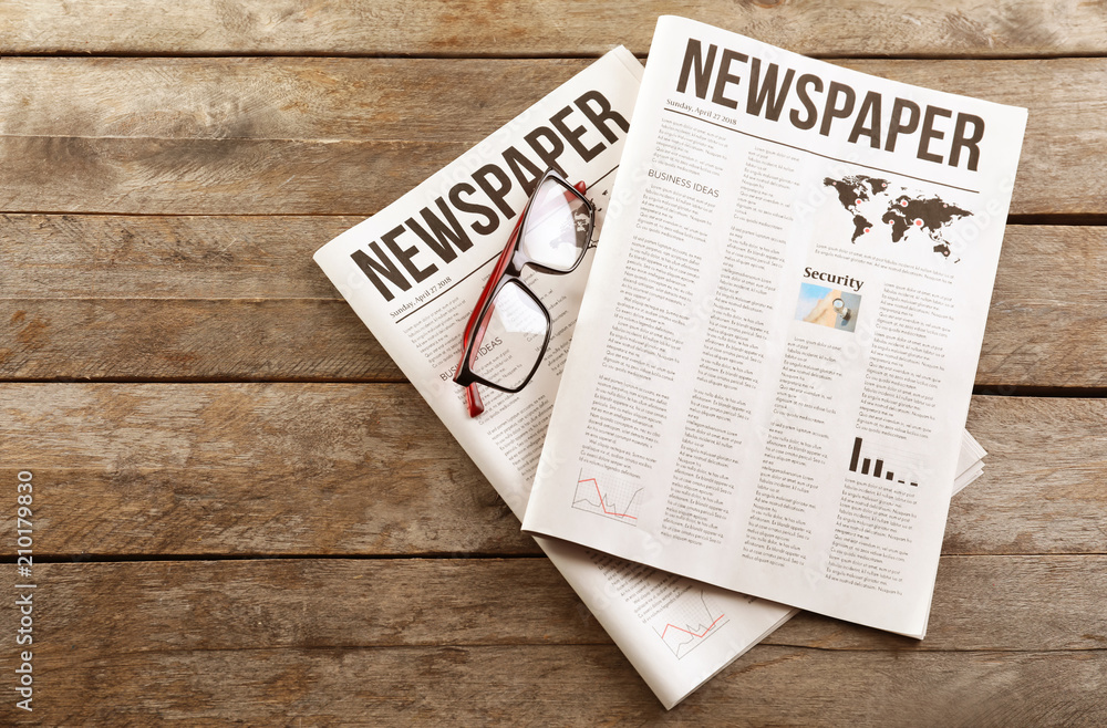 Newspapers with glasses on wooden background