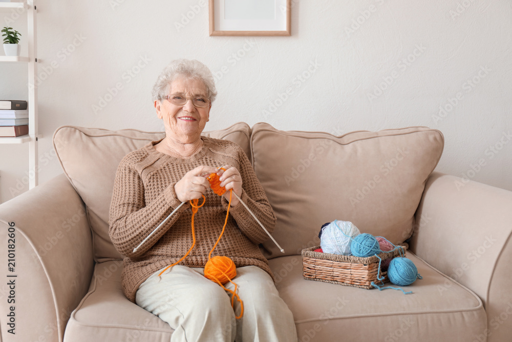 Senior woman sitting on sofa while knitting sweater at home