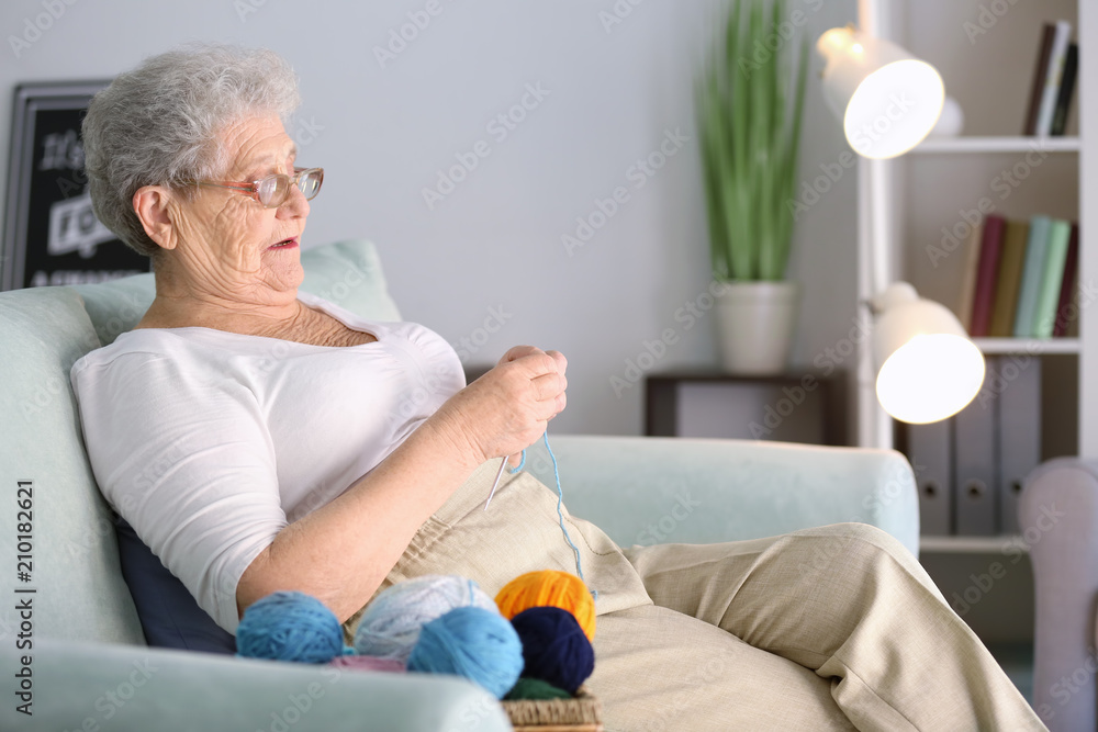 Senior woman sitting on sofa while knitting sweater at home