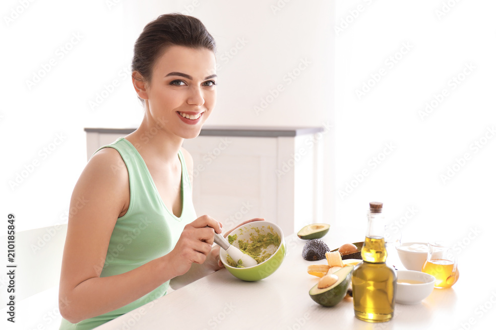 Young woman making nourishing mask with avocado in kitchen