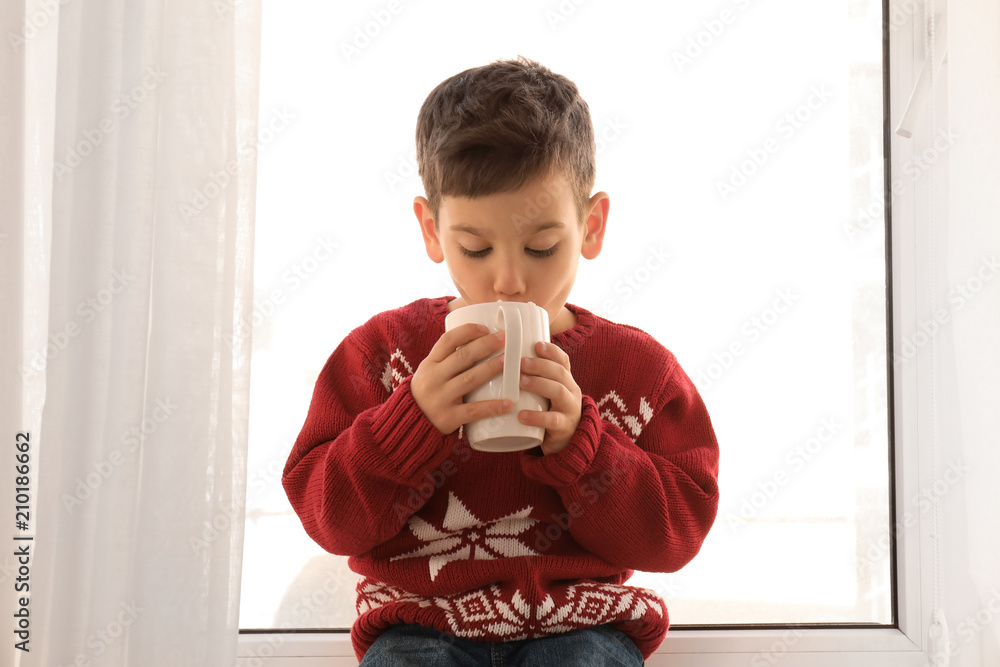 Cute little boy with cup of hot cocoa drink near window