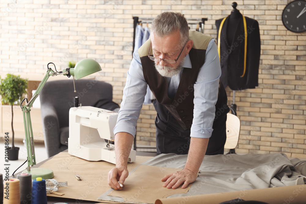 Mature tailor working with sewing pattern in atelier