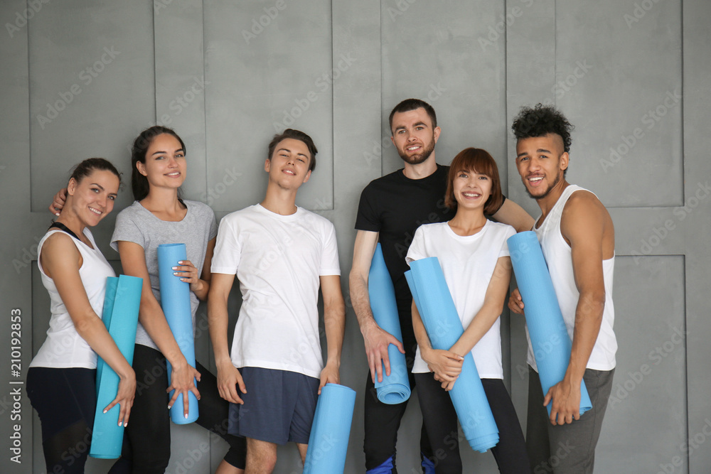 Group of sporty people with yoga mats near grey wall