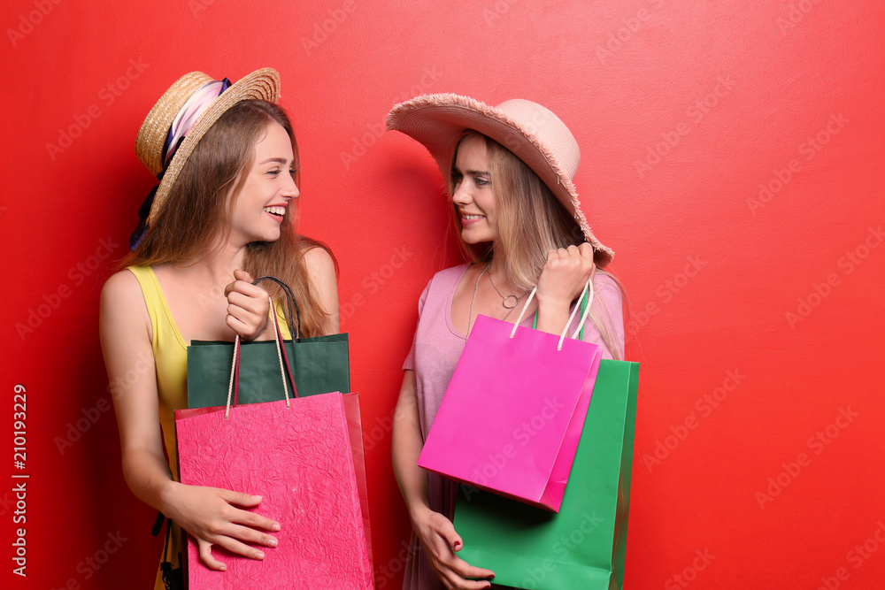 Beautiful young women with shopping bags on color background