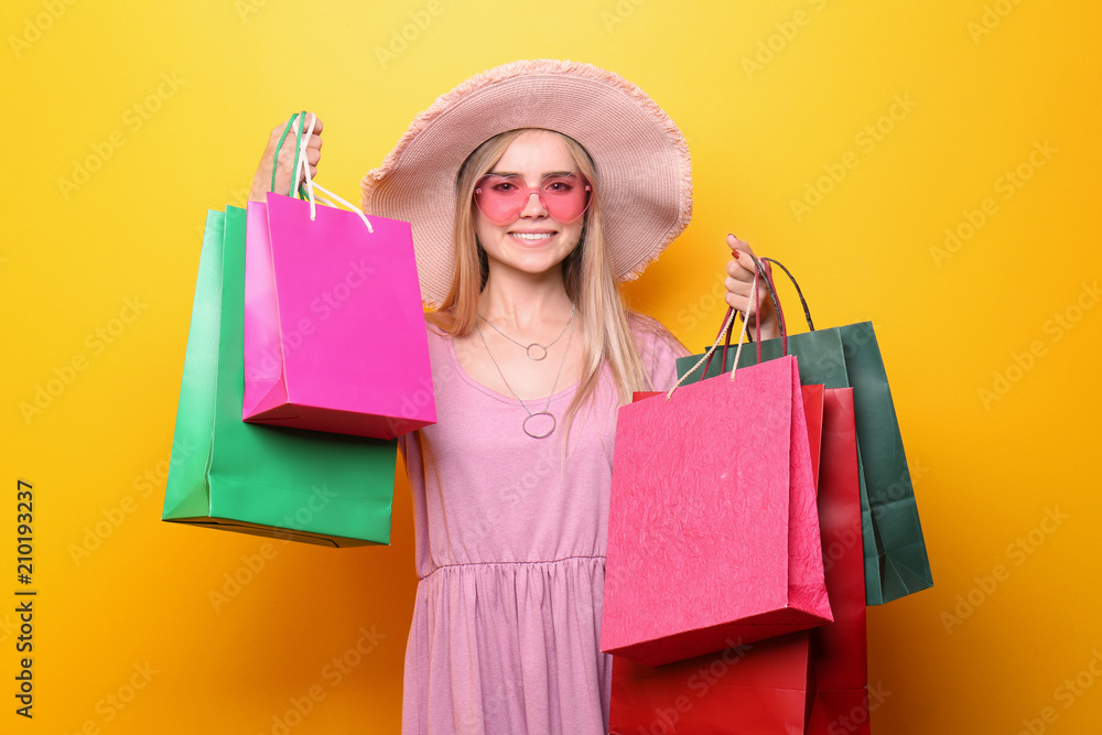 Beautiful young woman with shopping bags on color background