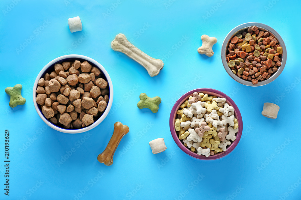 Bowls with pet food on color background