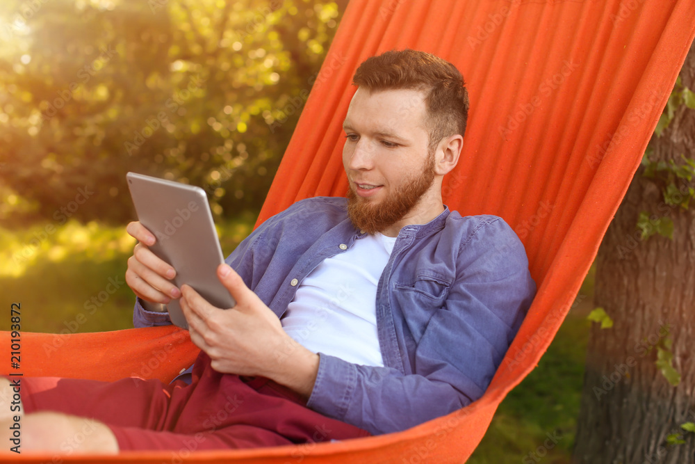 Young man with tablet computer in hammock outdoors