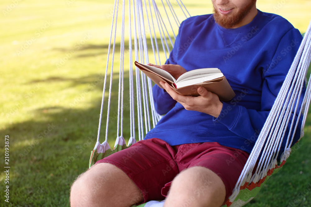 Young man reading book in hammock outdoors