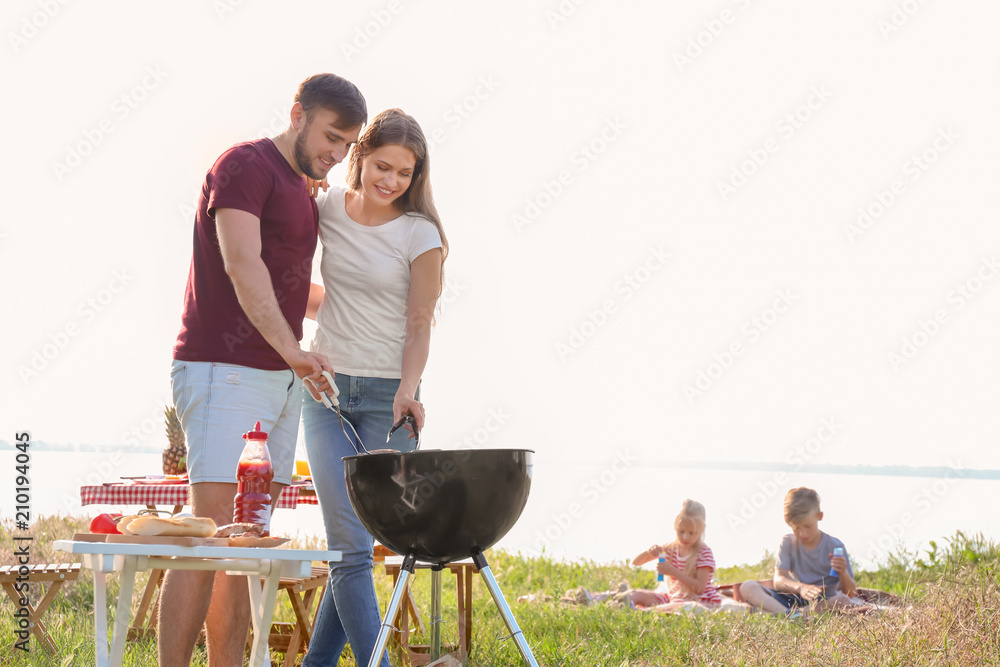 Happy young couple cooking tasty food on barbecue grill outdoors. Family picnic