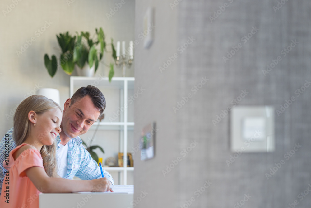 Young dad with a little daughter doing homework indoors