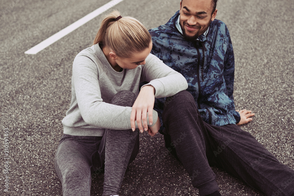 Smiling young couple sitting together on a road after running