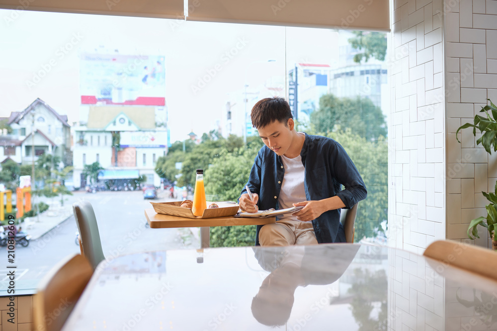 Handsome young designer writes creative graphic notes and making sketch in notebook while sitting at