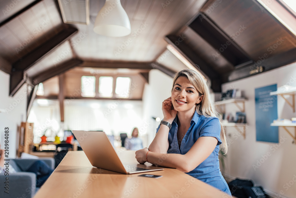 Portrait of a female entrepreneur in front of laptop in open space coworking office.