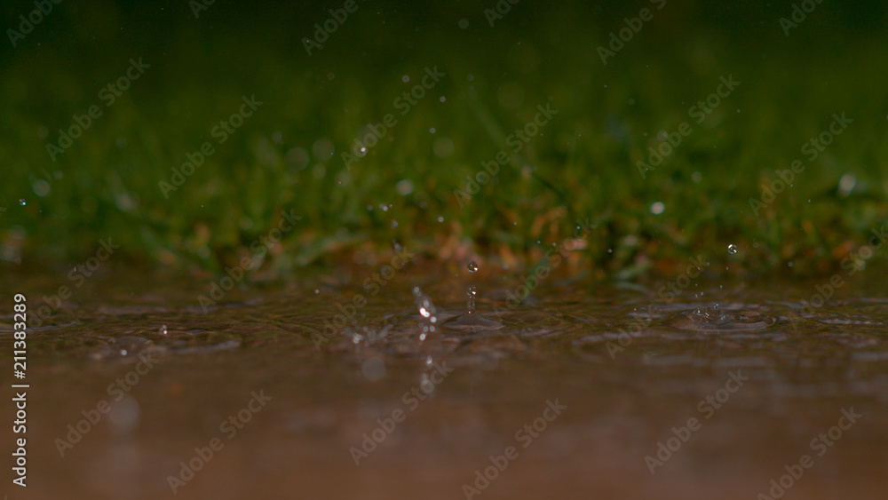 DOF: Crystal clear raindrops falling into murky puddle create a beautiful ripple