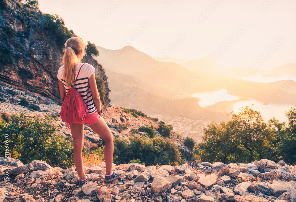 背着背包的年轻女子站在山上，日落时眺望海岸和山脉i