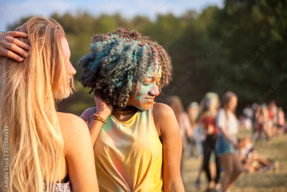 Two multiethnic girls covered in colorful powder dancing and celebrating summer holi festival