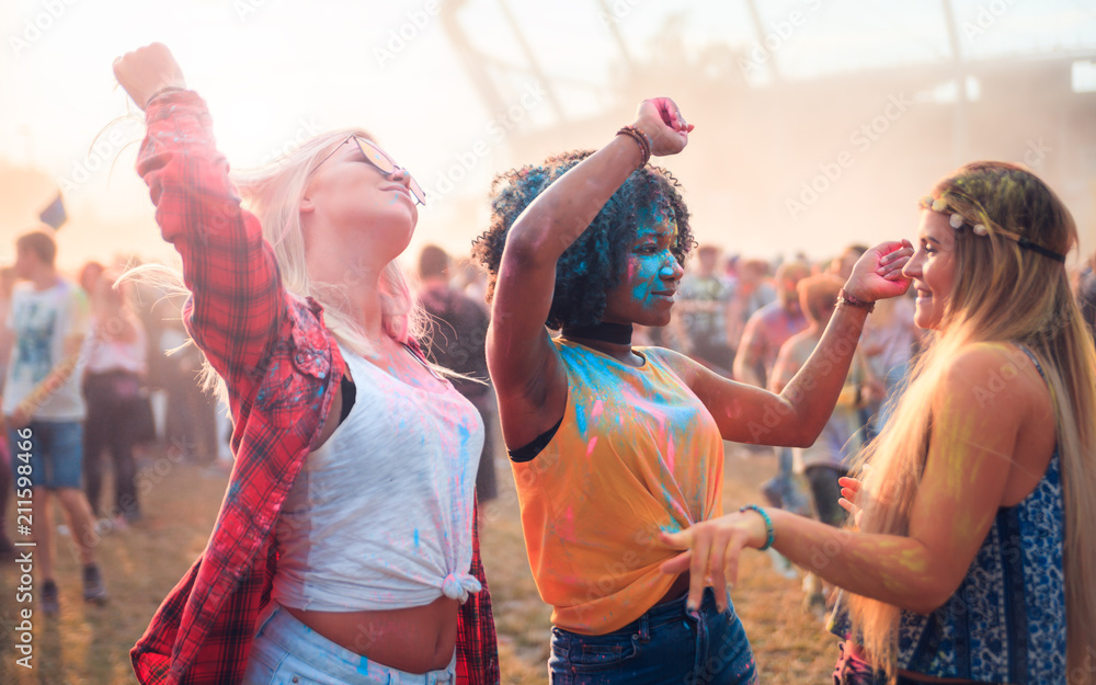 Multiethnic girls covered in colorful powder dancing and celebrating summer holi festival