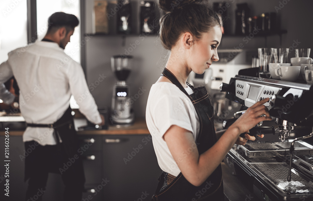 Young woman barista preparing coffee using machine in the cafe