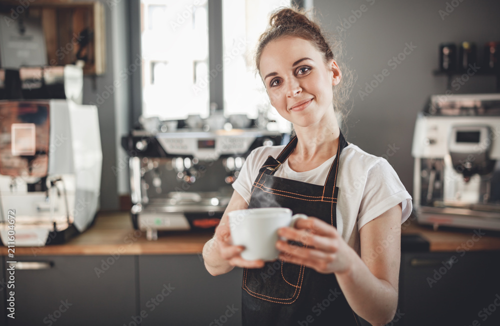 咖啡馆里一位职业咖啡师女士的画像，她裹着围裙，手里拿着一杯热咖啡