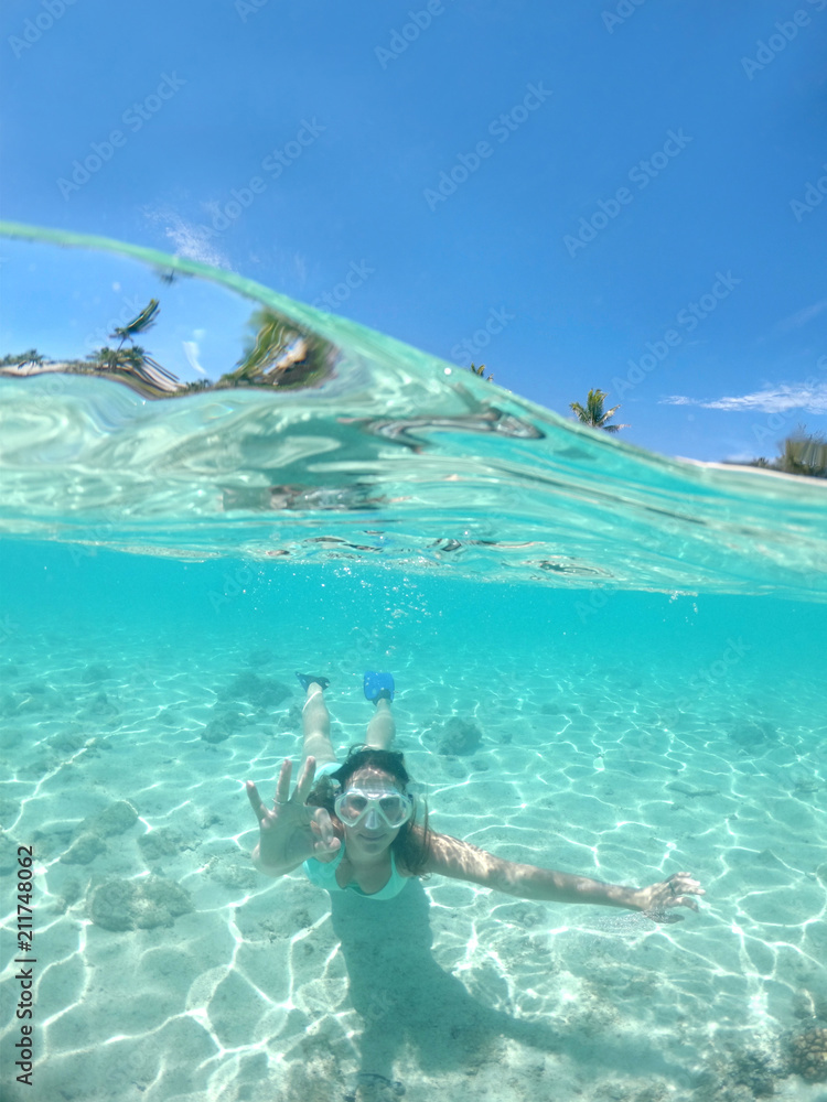 HALF UNDERWATER: Excited girl in bikini snorkeling in the beautiful ocean water.