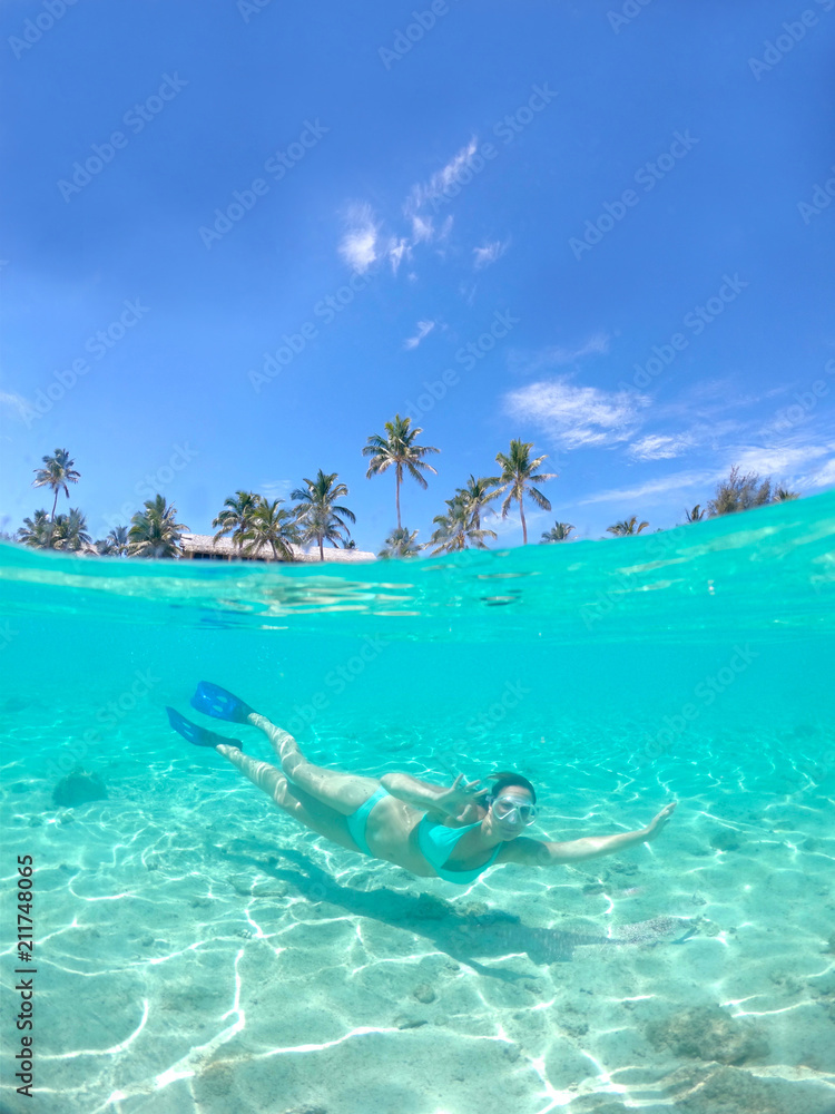 HALF UNDERWATER: Traveler swims sideways and gives the ok sign with her hand.