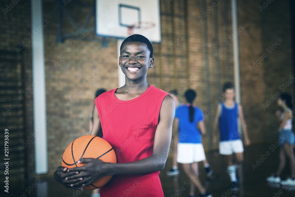 Smiling school boy holding a basketball while team playing in