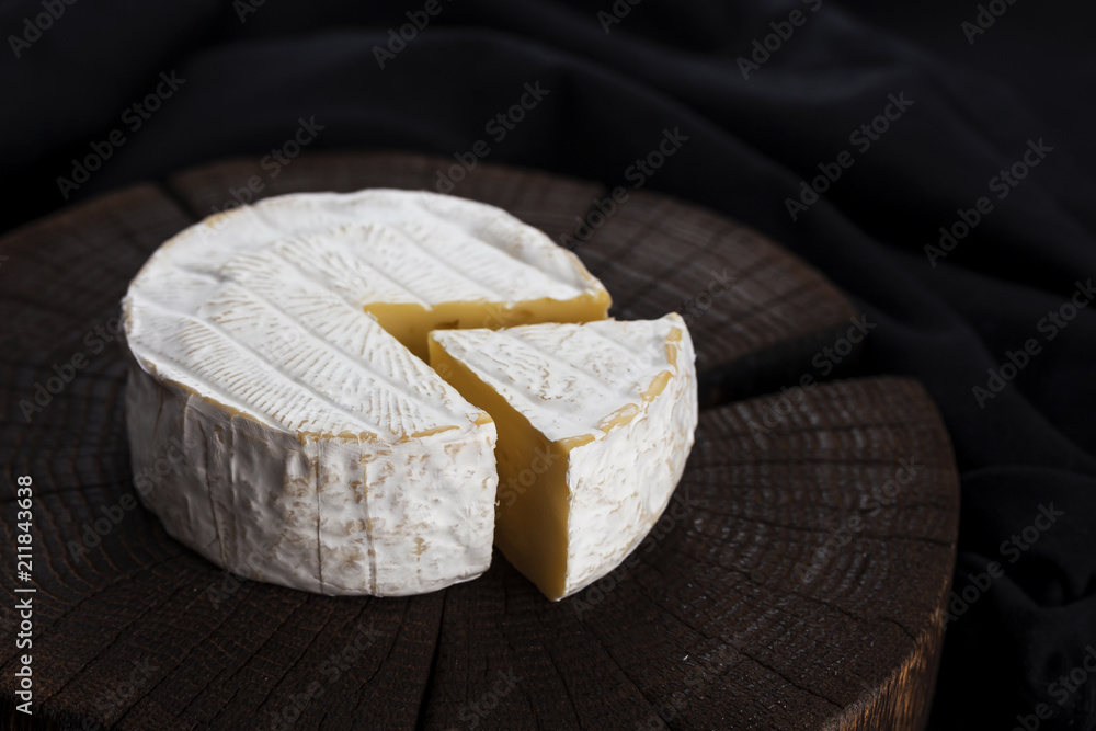 Camembert cheese on black wooden background, with copy space. Shallow depth of field