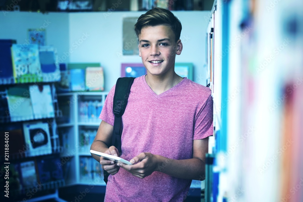 Portrait of happy schoolboy holding digital tablet in library